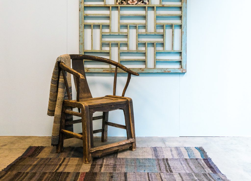 Antique horse shoe chair on an ancient carpet from the Yao minority tribe, and a decorative old wooden panel on the wall