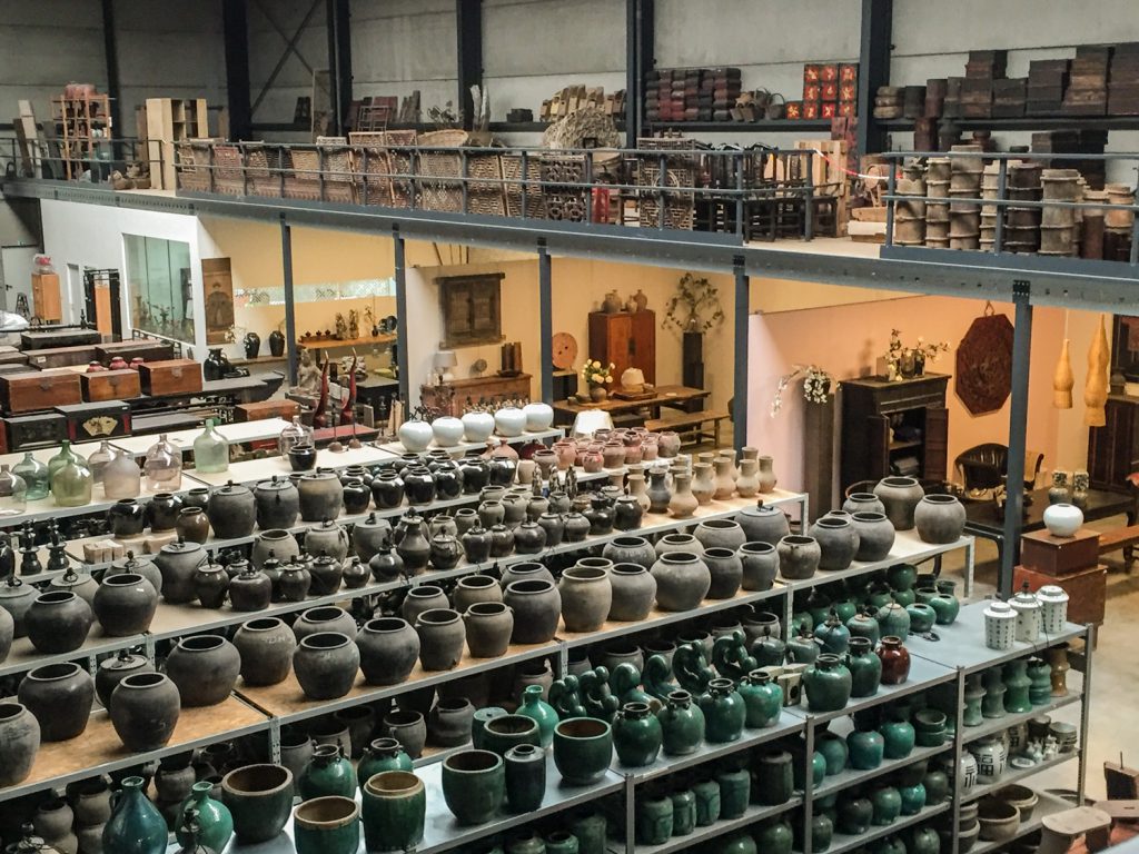 Het magazijn van de Zijderoute Collectie met veel antieke meubels en stapels antieke potten