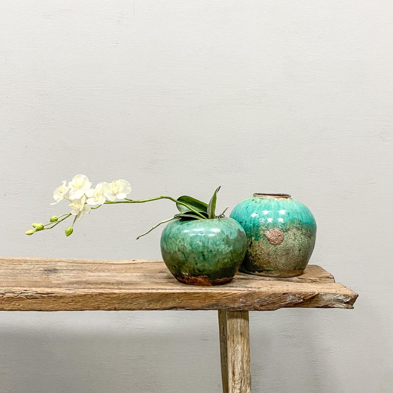 Antique turquoise ginger pot with decorative flowers standing on a weathered Chinese wooden bench